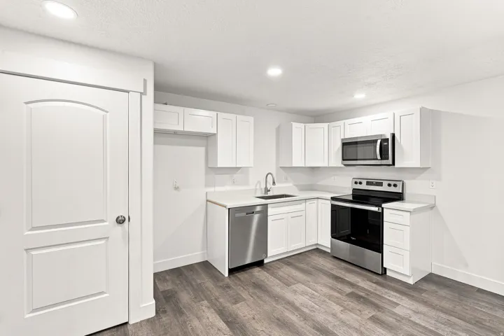 White shaker cabinetry, stainless steel appliances, wood-finish flooring, recessed lighting, and a subway tile backsplash