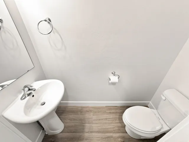 Pedestal sink with chrome faucet, wall-mounted mirror, white toilet, and wood-finish flooring