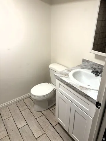 Compact half bathroom featuring a white ceramic pedestal sink with chrome fixtures, a toilet with a closed lid, and wood-finish plank flooring