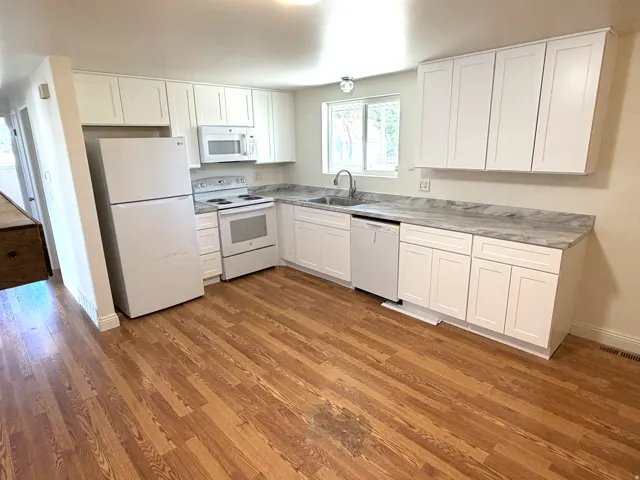 Kitchen featuring white cabinetry, wood-finish flooring, white appliances, laminate countertops, and a stainless steel sink with a window above