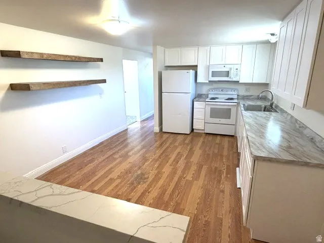 Kitchen featuring white cabinetry, white appliances, wood-finish flooring, and light-toned countertops