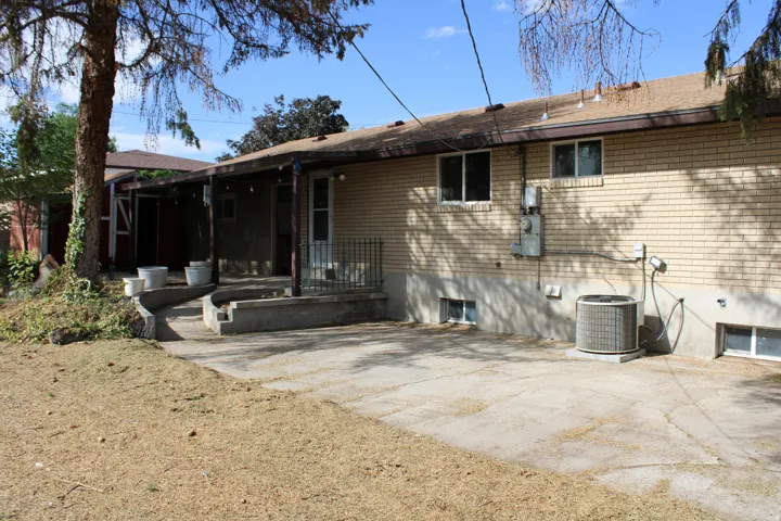 Brick exterior with a covered patio, concrete patio, and mature trees