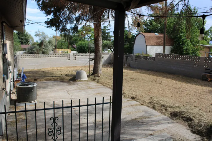 Expansive backyard featuring a concrete patio, mature trees, and a block fence