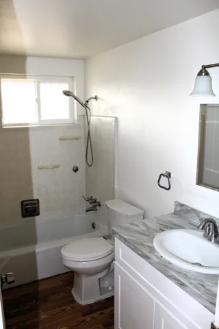 White vanity with a single basin sink, wood-finish flooring, and a white bathtub with tile surround