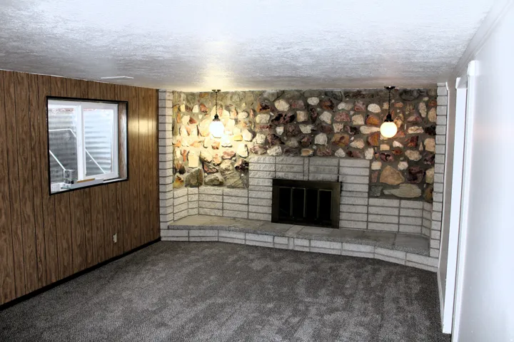 Stone-faced fireplace with a raised brick hearth, wood-paneled accent wall, and recessed window
