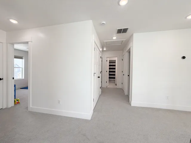 Recessed ceiling lighting, white walls, light gray carpeting, multiple white doors with black hardware, and a white trim finish