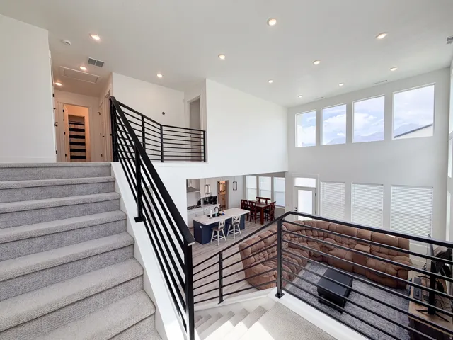 High ceilings with recessed lighting, black horizontal bar railing, large windows, wood-finish flooring, and a kitchen island with seating