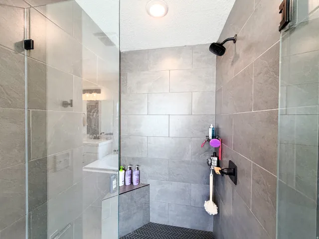 Glass-enclosed shower with full-height tile surround, built-in shelving, matte black fixtures, and a herringbone-patterned floor