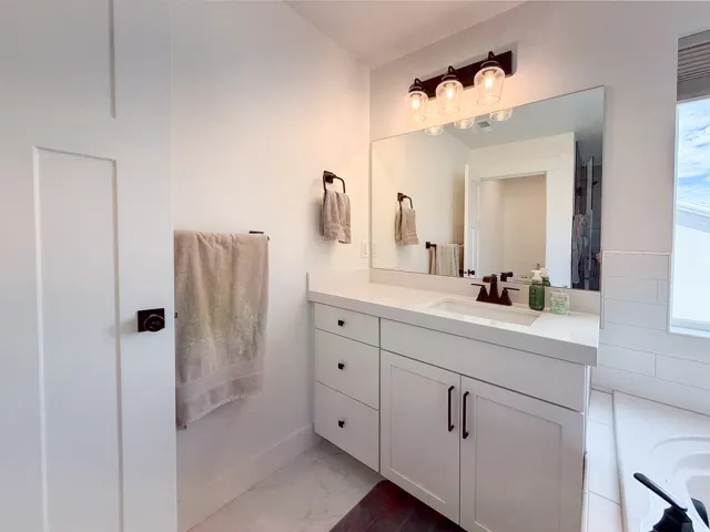 White vanity with a single basin sink, light-toned countertop, dark bronze fixtures, and an integrated lighting fixture