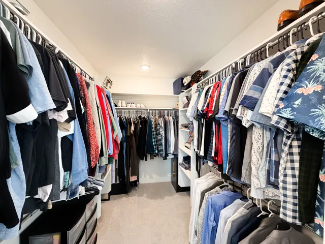 Built-in closet system with multiple hanging rods, dedicated shelving, and soft carpet flooring