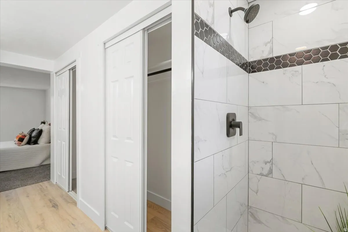 Shower featuring large format white tiled walls with subtle veining, dark hexagonal accent tile, and matte black fixtures
