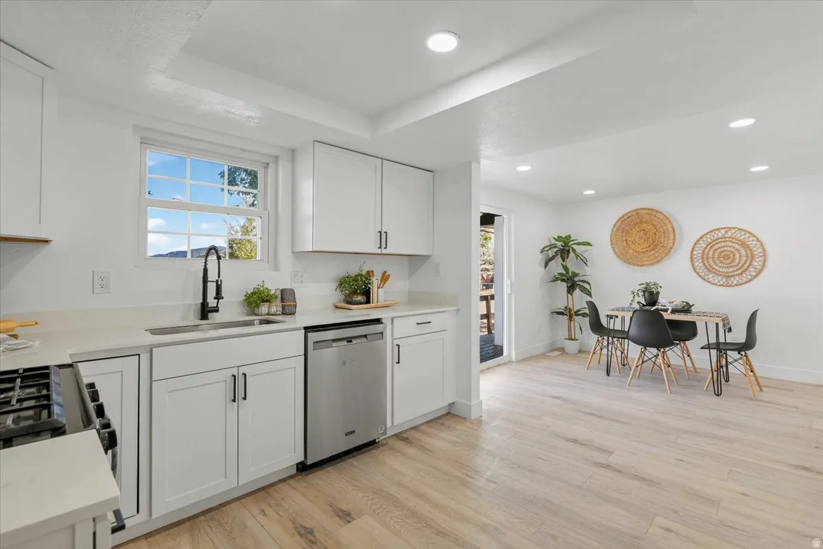 Kitchen featuring white shaker cabinetry, stainless steel dishwasher, black faucet, light stone countertops, and wood-finish flooring