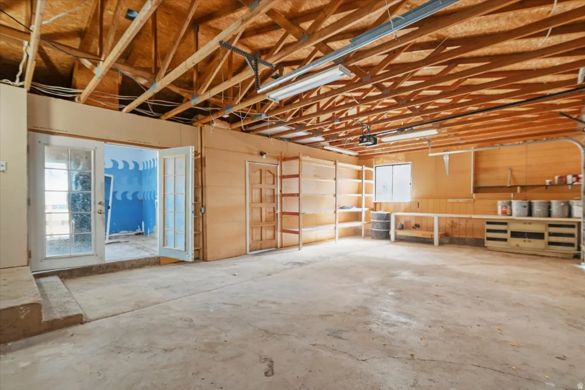 Oversized garage with concrete flooring, built-in shelving, work surfaces, and double French doors with glass panels