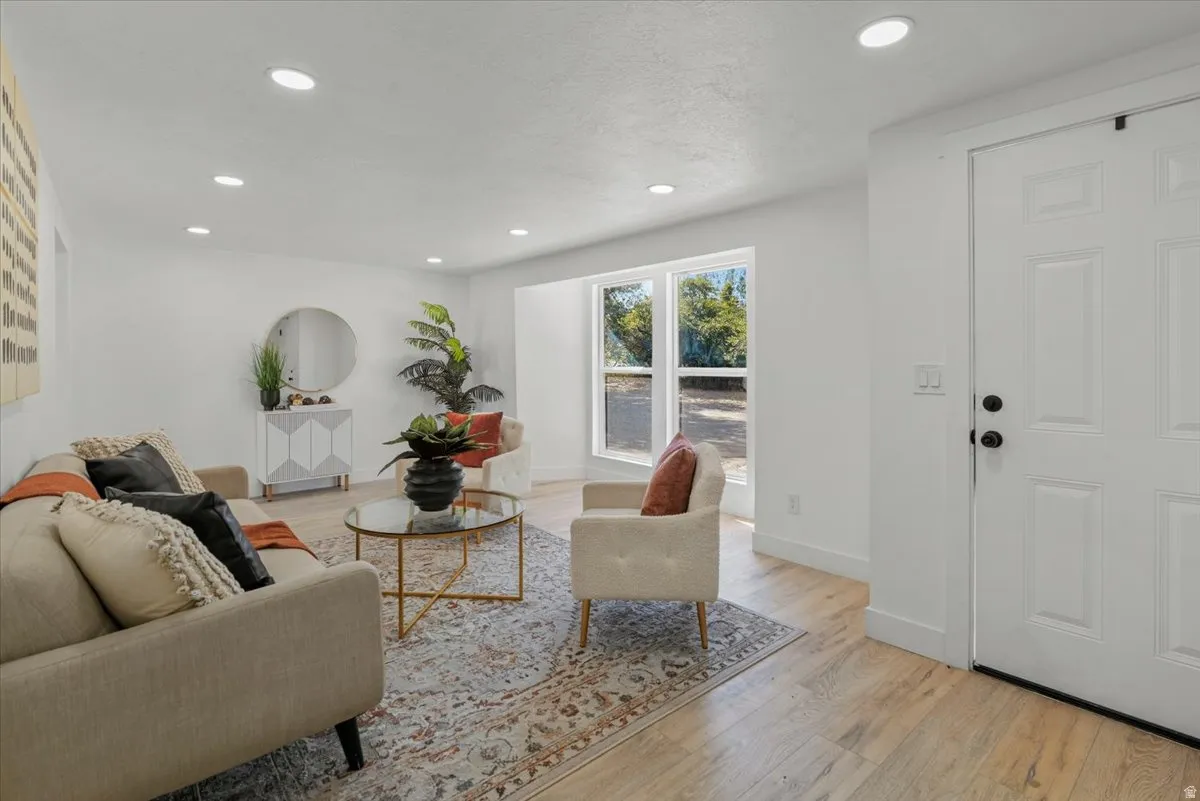 Recessed lighting, wood-finish flooring, white paneled entry door, multiple windows, and light-toned walls