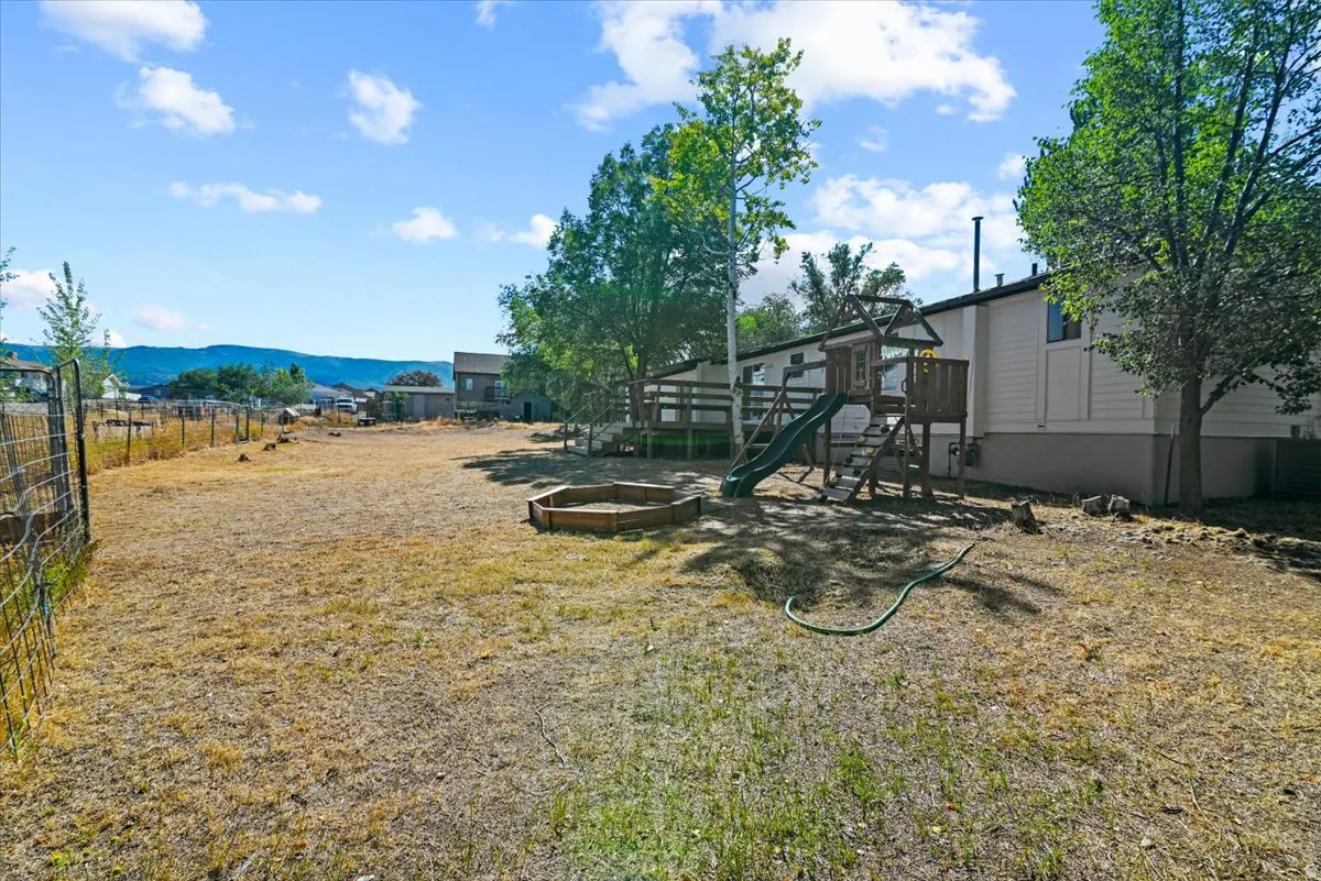 Expansive backyard featuring a fenced perimeter and a wooden playset with a slide