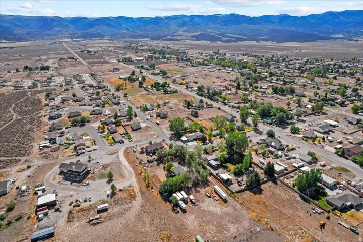 Aerial perspective showcasing scattered residential properties, mature trees, and mountainous terrain in the background
