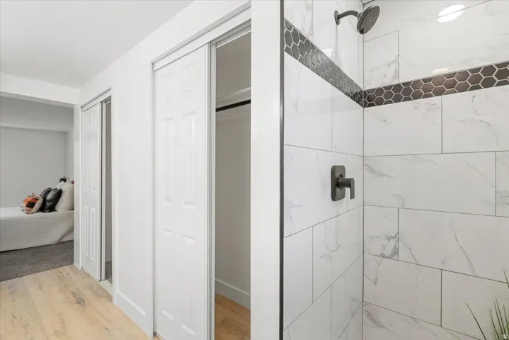 Shower featuring large format white tiled walls with subtle veining, dark hexagonal accent tile, and matte black fixtures