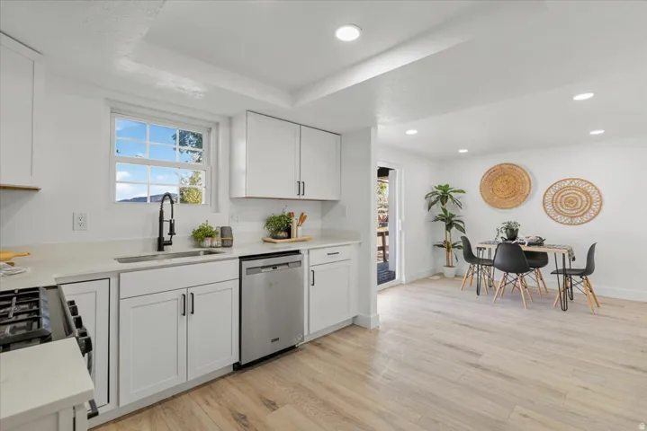 Kitchen featuring white shaker cabinetry, stainless steel dishwasher, black faucet, light stone countertops, and wood-finish flooring