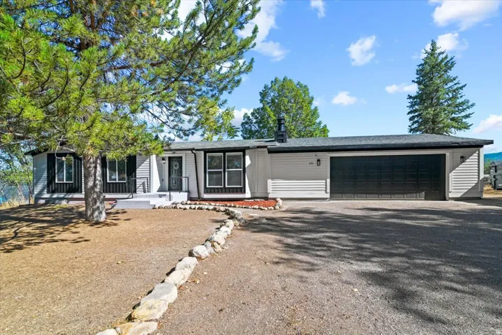 Single-story residence featuring light-toned siding, black-framed windows, an attached garage with a black door, and a stone-lined pathway