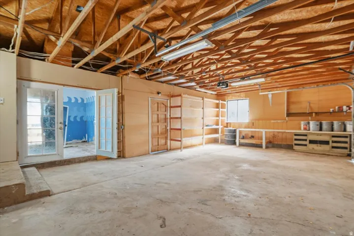 Oversized garage with concrete flooring, built-in shelving, work surfaces, and double French doors with glass panels