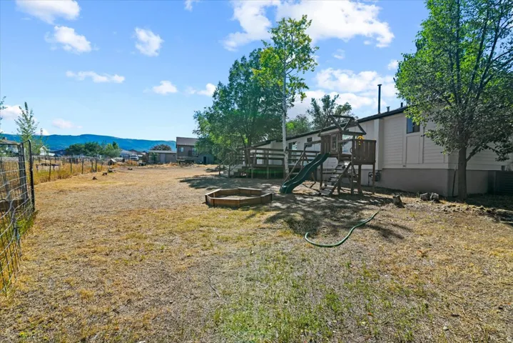 Expansive backyard featuring a fenced perimeter and a wooden playset with a slide