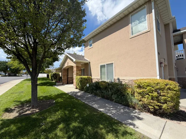 Stucco exterior with stone veneer accents, covered entry, manicured landscaping, and a concrete walkway