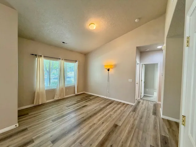Vaulted ceiling, wood-finish flooring, multiple windows, recessed lighting, and a neutral color palette