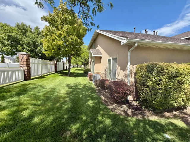 Expansive green lawn with mature trees and a white privacy fence with stone pillars