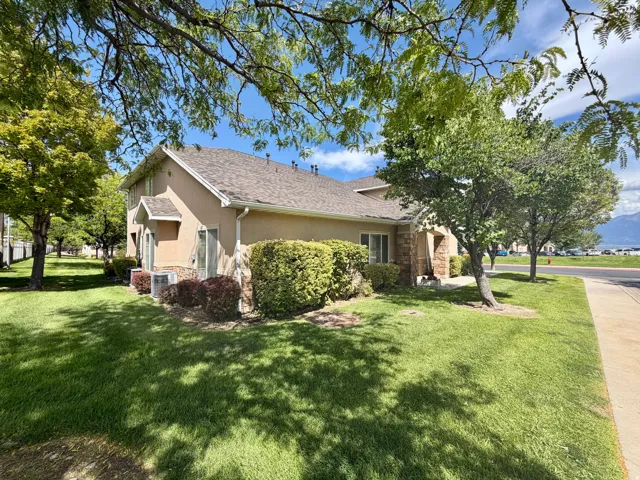 Stucco exterior with stone accents, featuring a shingled roof and mature landscaping with established trees and shrubs