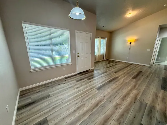 Vaulted ceiling with an overhead light fixture, wood-finish flooring, and multiple windows with blinds