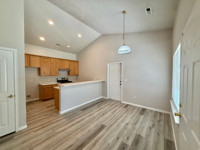Vaulted ceilings with recessed lighting, wood-finish flooring, kitchen with wood cabinetry and light countertops, and a white paneled door