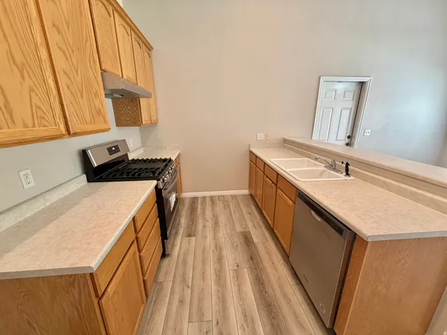Kitchen featuring wood-finish cabinetry, light-toned countertops, stainless steel appliances, and wood-finish flooring