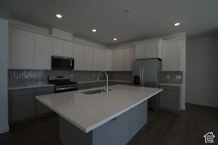 Kitchen featuring a large central island, stainless steel appliances, two-tone cabinetry, a tile backsplash, and recessed lighting