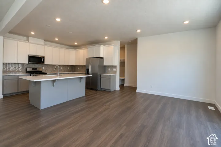 Kitchen featuring an island with a light-colored countertop, stainless steel appliances, and a tile backsplash