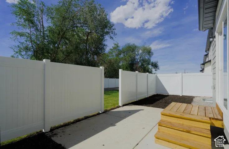 Private outdoor area featuring a wood staircase, concrete patio, white privacy fencing, and a manicured lawn