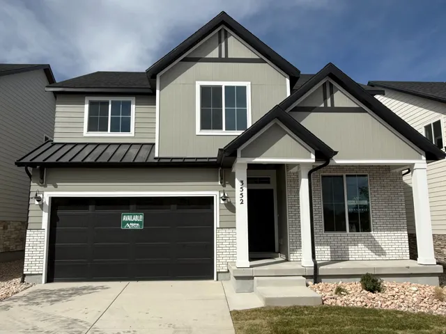 Two-story residence featuring light gray siding, white brick accents, a dark gray garage door, and a covered entry porch supported by white columns