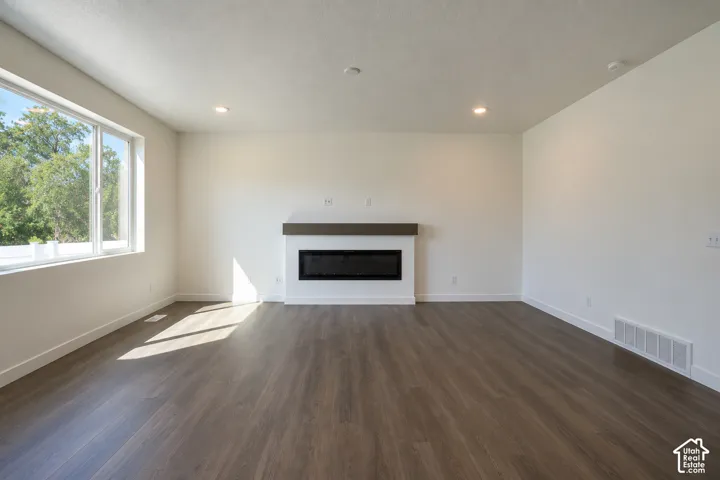 Spacious room with wood-finish flooring, large multi-pane window, built-in linear fireplace, wood mantel, and recessed lighting