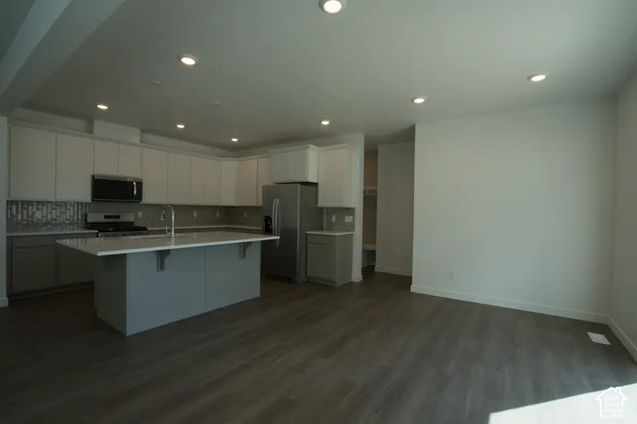 Kitchen featuring an island with a breakfast bar, stainless steel appliances, upper and lower cabinetry, and a full-height backsplash