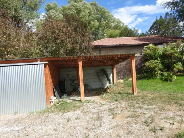 Attached shed with a corrugated metal exterior, an open-sided wood frame structure, and a gravel-covered ground area