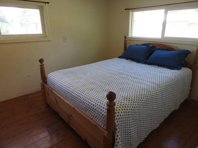 Spacious bedroom featuring hardwood flooring, wooden bed frame with turned posts, dual windows with natural light, and neutral wall finishes