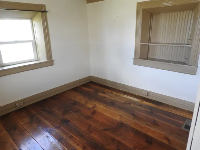 Bright corner bedroom featuring hardwood flooring, dual windows with natural light, and clean white walls