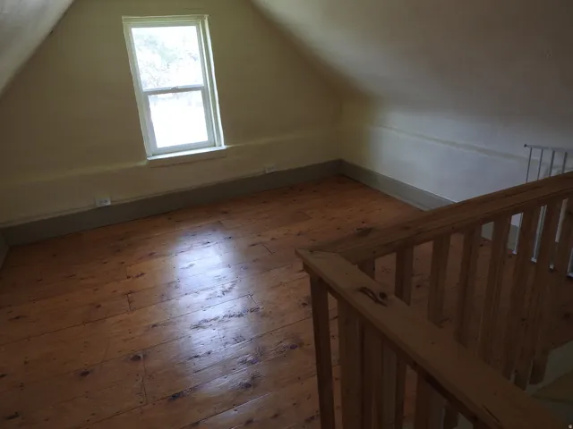 Natural wood flooring with a warm finish, sloped attic ceiling, and a single pane window