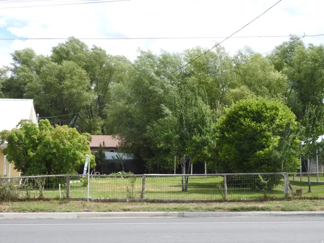 Grassed lot with partial wood and wire fencing, bordered by mature trees