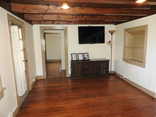 Spacious room featuring exposed wooden beam ceiling with recessed lighting, rich wood-finish flooring throughout, and multiple doorway entries