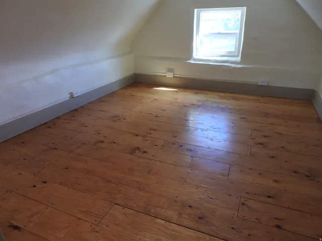 Wood-finish flooring with visible fasteners and a white window frame