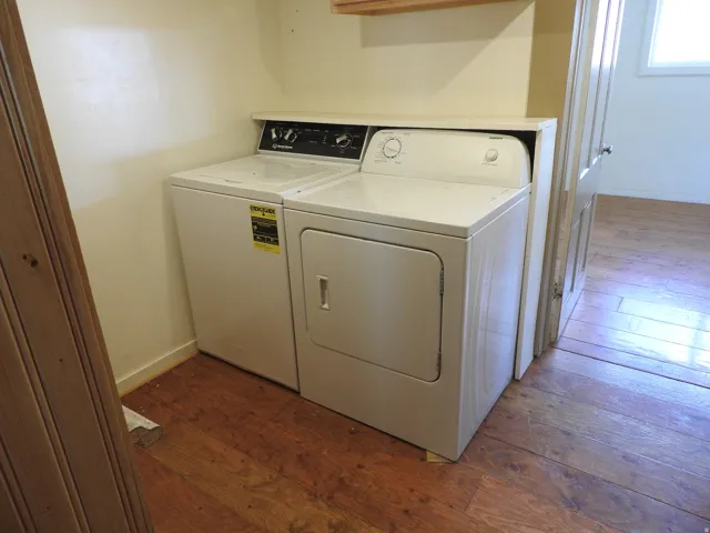 Dedicated laundry room featuring side-by-side washer and dryer with top-mounted controls, wood-finish flooring, and ample counter space above appliances for folding and sorting