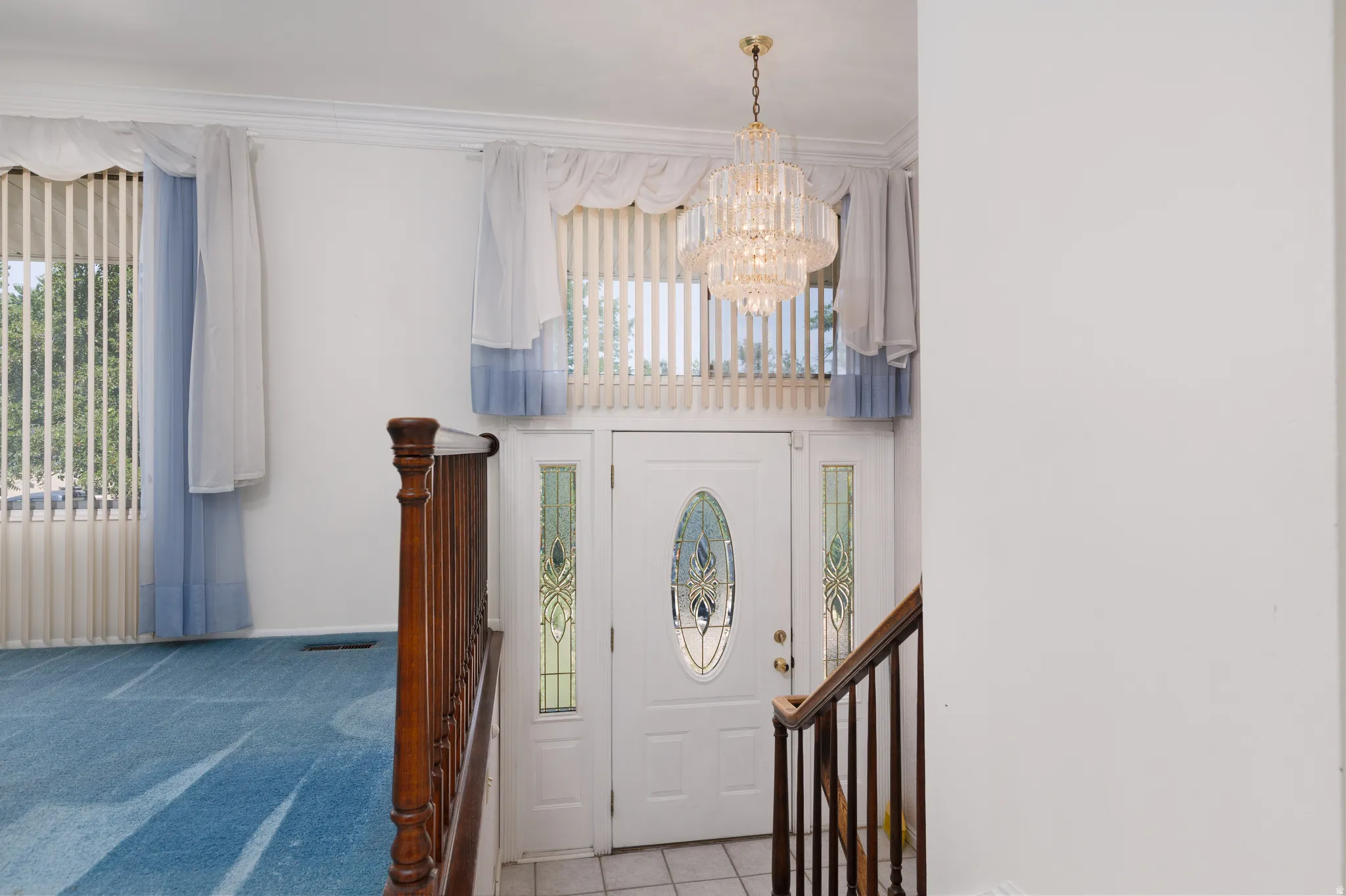 Entryway featuring a decorative front door with an oval glass insert and side lites, a tiered chandelier, and a wood staircase