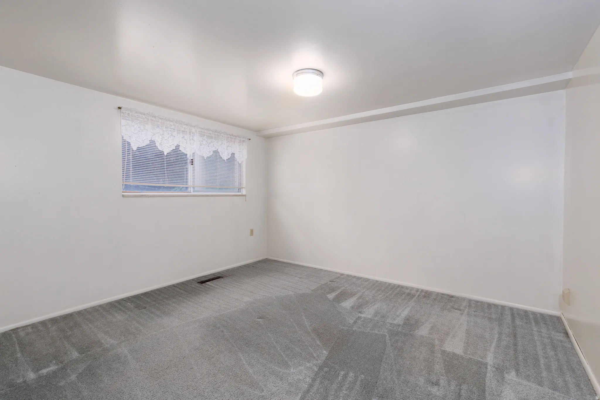 Carpeted room with white walls, a single window, and an overhead flush-mount light fixture