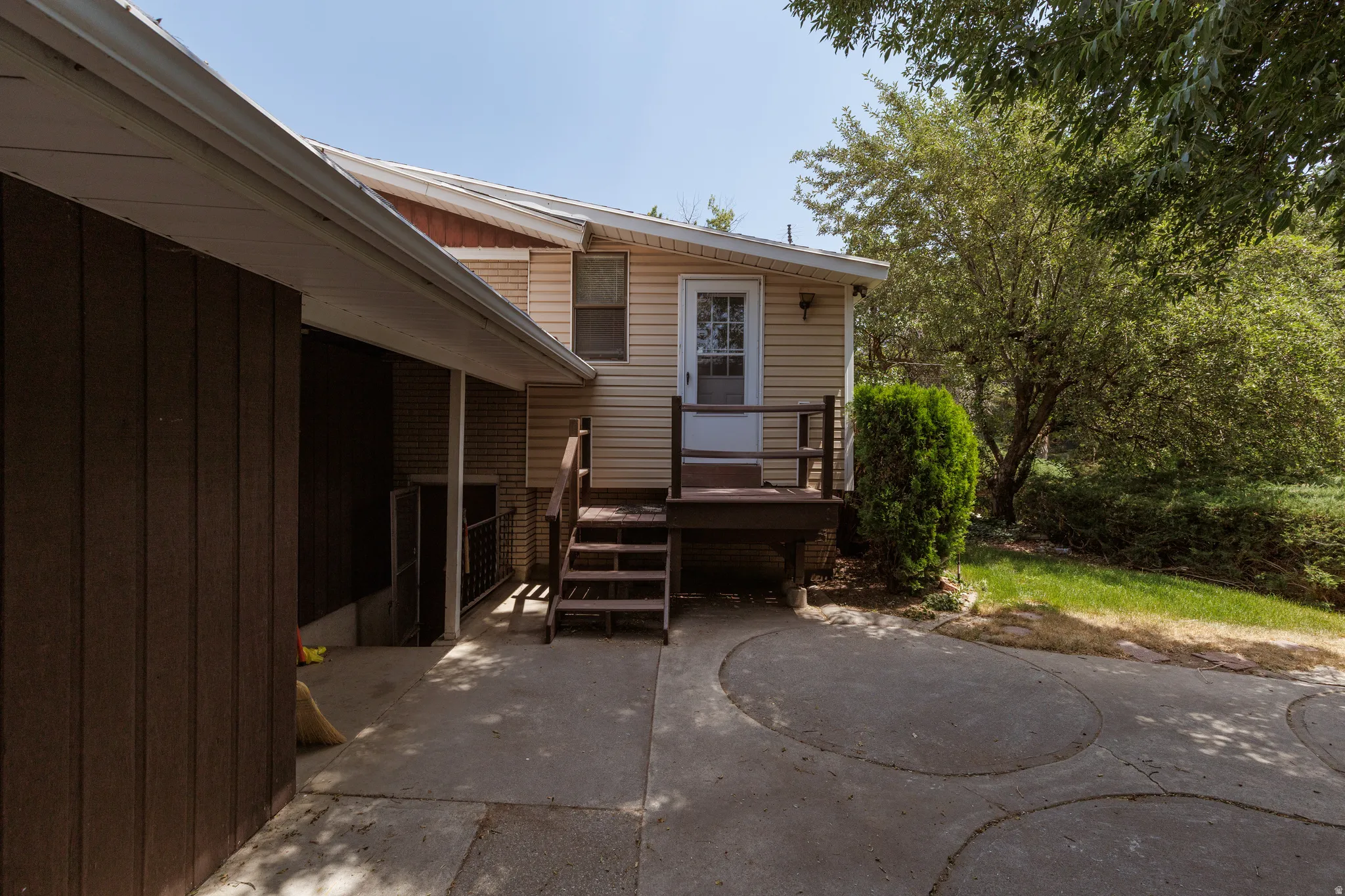 Rear exterior featuring tan siding, a brown wood deck, and a glass-paneled door