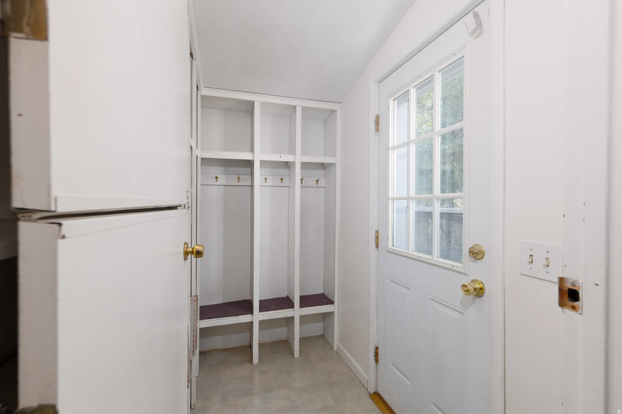 Entryway with built-in cubby storage, white shaker-style door with glass pane, brass-finish hardware, and light-toned flooring